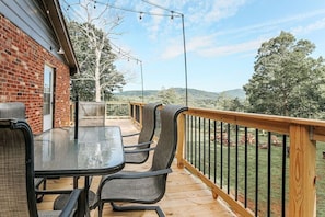 Une terrasse avec une table et des chaises en verre, un mur en briques et une vue sur un paysage vallonné.