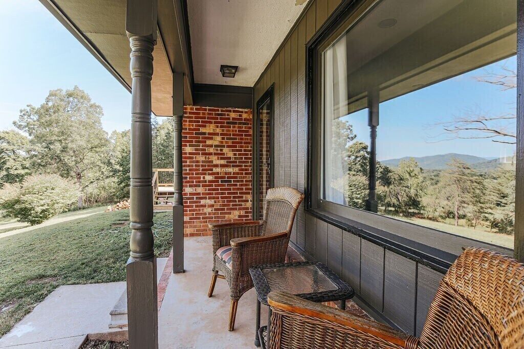 A covered porch with wicker furniture, a brick wall, and a view of a green landscape.