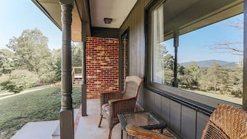 A covered porch with wicker furniture, a brick wall, and a view of a green landscape.