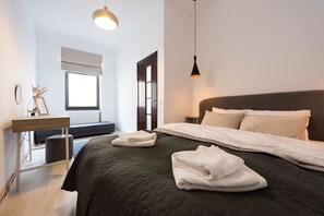 A modern bedroom with a large bed, bedside tables, a window with blinds, and a hanging light fixture. - Charming family sized flat in the heart of Brasov Old Town (Brasov)