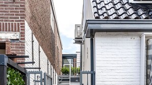 Una terraza de madera estrecha que conduce a un edificio de ladrillo blanco con un portón negro y el número '3' en la pared.