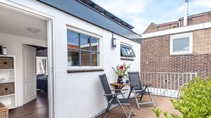 Una casa moderna con terraza de madera, zona de comedor con sillas, una mesa pequeña y un jarrón de flores.