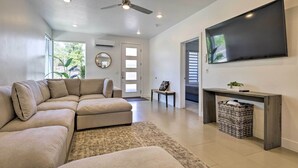 Un salon moderne avec un canapé d’angle, un téléviseur à écran plat, un ventilateur de plafond et une grande fenêtre.