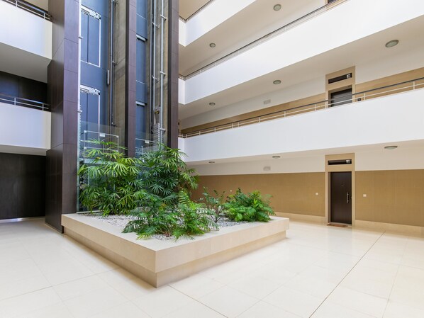 A spacious indoor atrium with a central planter with various plants, multiple floors with balconies, and a modern architectural design. - Apartment Henri - Perfect couples getaway! (Lagos)