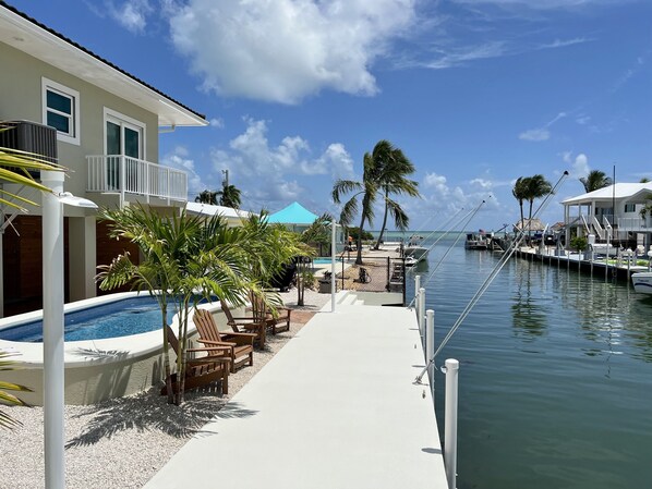 A marina with boats docked, a swimming pool with lounge chairs, and a building with a balcony.