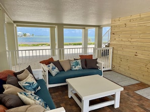 A covered outdoor seating area with a view of the ocean, a white table, and a wooden wall.