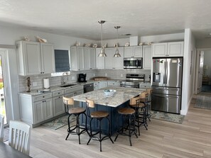 A modern kitchen with white cabinets, stainless steel appliances, and a central island with bar stools.