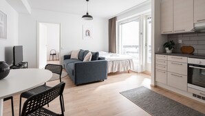 A modern apartment with a dining area, a sofa, a kitchen, and a large window. - 1BR & Balcony next to Railway Station (Tampere)