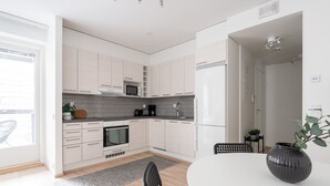 A modern kitchen with white cabinets, a microwave, and a refrigerator. There is a dining table with chairs and a vase of flowers. - 1BR & Balcony next to Railway Station (Tampere)
