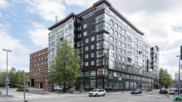 A modern multi-story building with a mix of residential and commercial spaces, featuring large windows and a prominent entrance. - 1BR & Balcony next to Railway Station (Tampere)