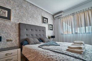 Une chambre à coucher avec une tête de lit capitonnée, une couvre-lit à motifs et une table de chevet avec une lampe.