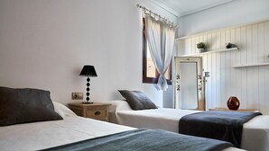 A room with two beds, a nightstand with a lamp, a door with a floral design, and a shelf with plants. - Casa Anna, modern with rustic design (Costa Calma)