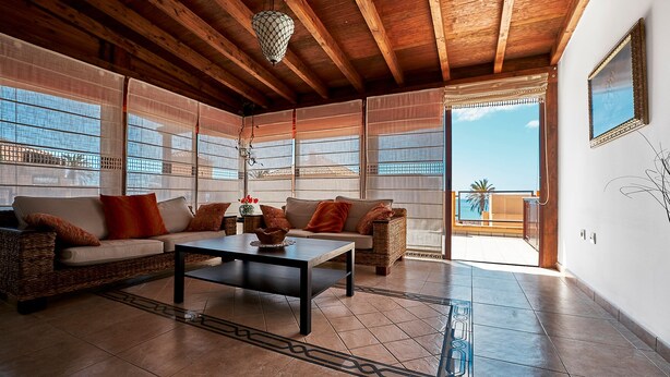 A spacious living area with a wooden ceiling, large windows, a sofa set, and a dining table. - Casa Anna, modern with rustic design (Costa Calma)