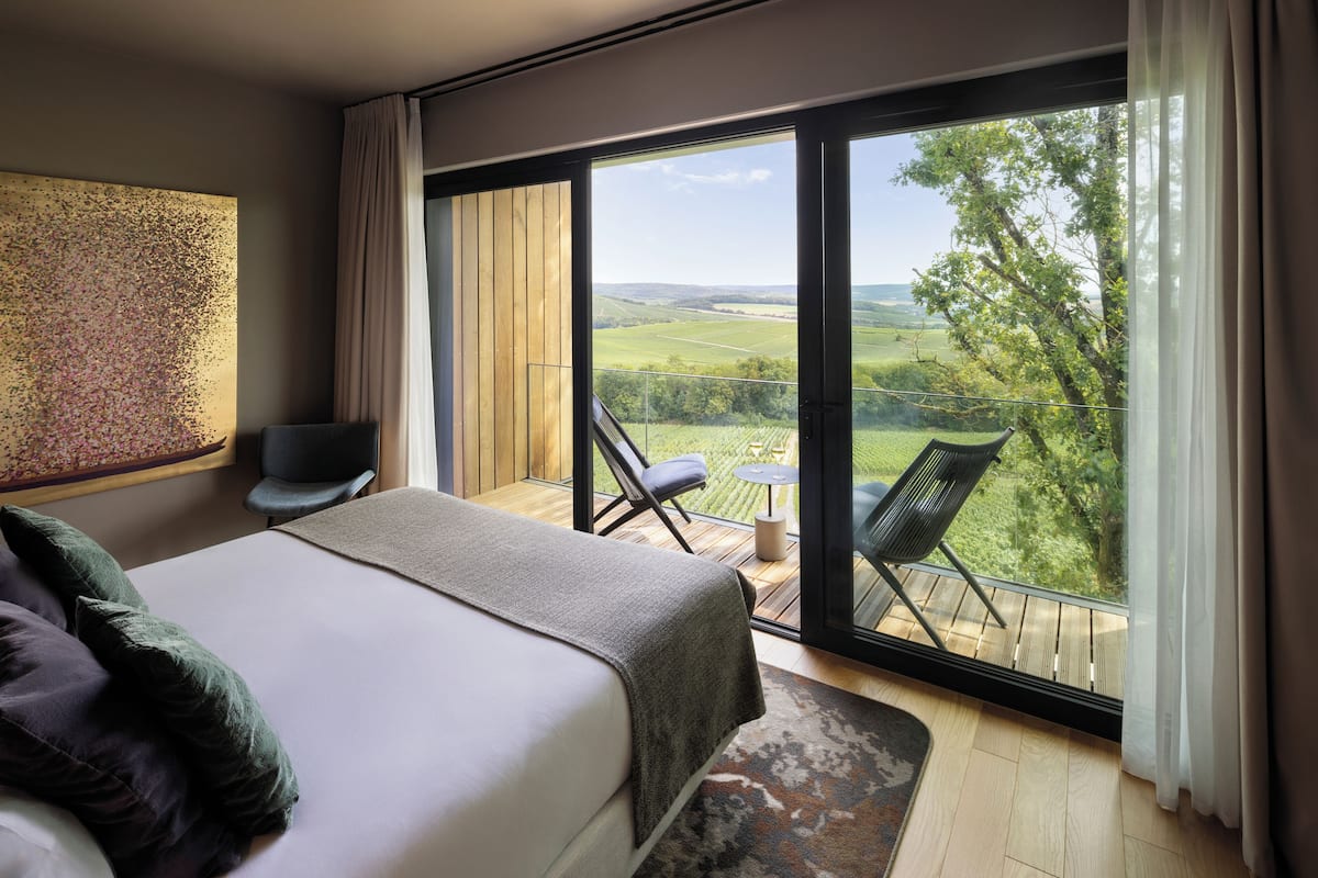 Een slaapkamer met een groot bed, een stoel en een balkon met uitzicht op het platteland.