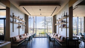 Ein Restaurant mit hohen Tischen und Bänken, großen Fenstern und Regalen mit verschiedenen Gegenständen.