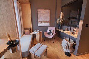 Ein modernes Zimmer mit Bett, kleinem Tisch, Stuhl, Nachttisch mit Lampe und Fenster mit Blick.