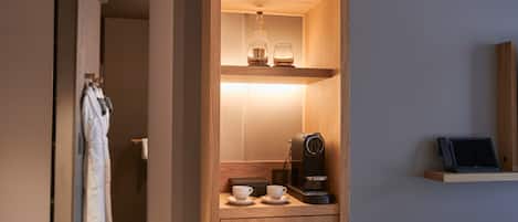 A compact hotel room with a wooden cabinet, a coffee machine, and a laptop on a shelf.