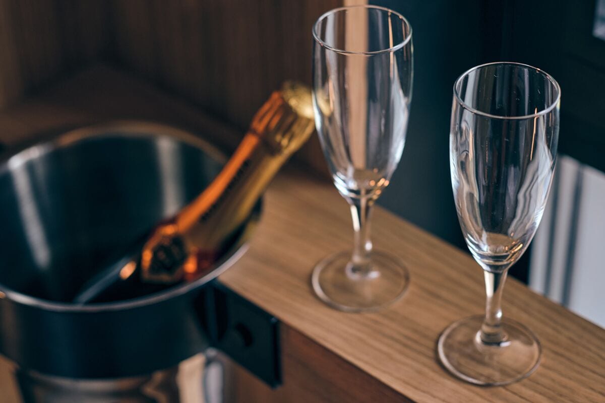 A metallic bucket with a golden handle on a wooden surface, accompanied by two clear wine glasses.