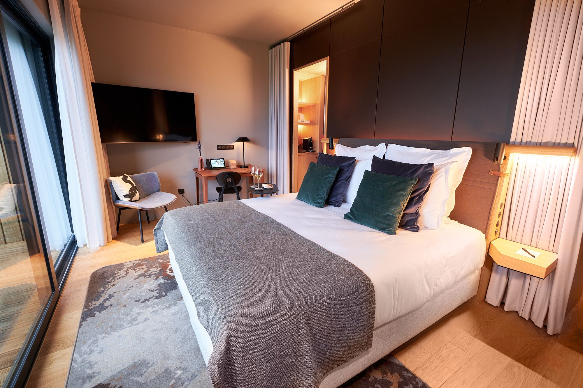Habitación de hotel moderna con una cama grande, un escritorio, una silla, un televisor y vistas a la ciudad.