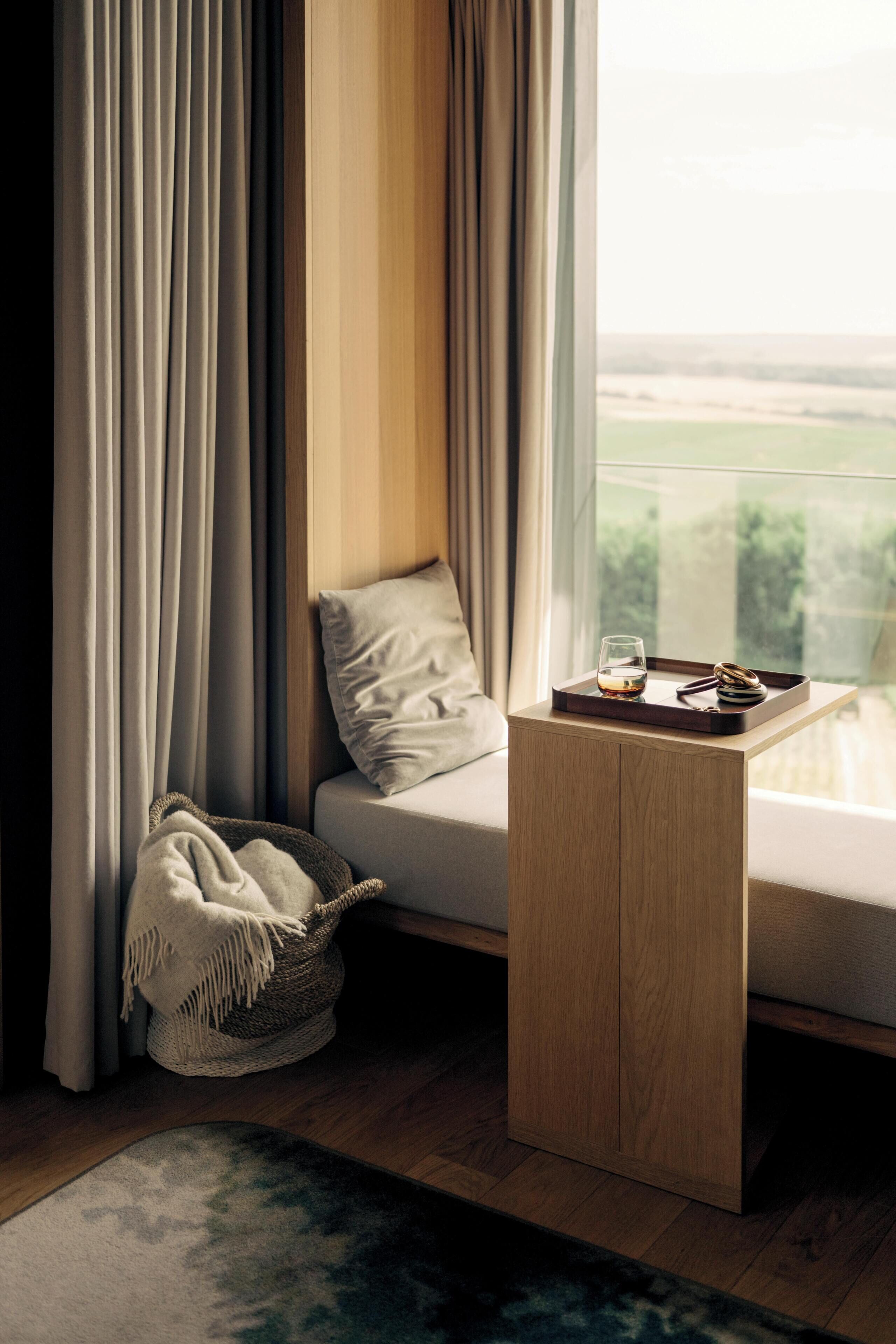 A modern room with a sofa, a small wooden side table, a glass of whiskey, and a tray with a bottle and a glass.