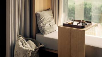 A modern room with a sofa, a small wooden side table, a glass of whiskey, and a tray with a bottle and a glass.