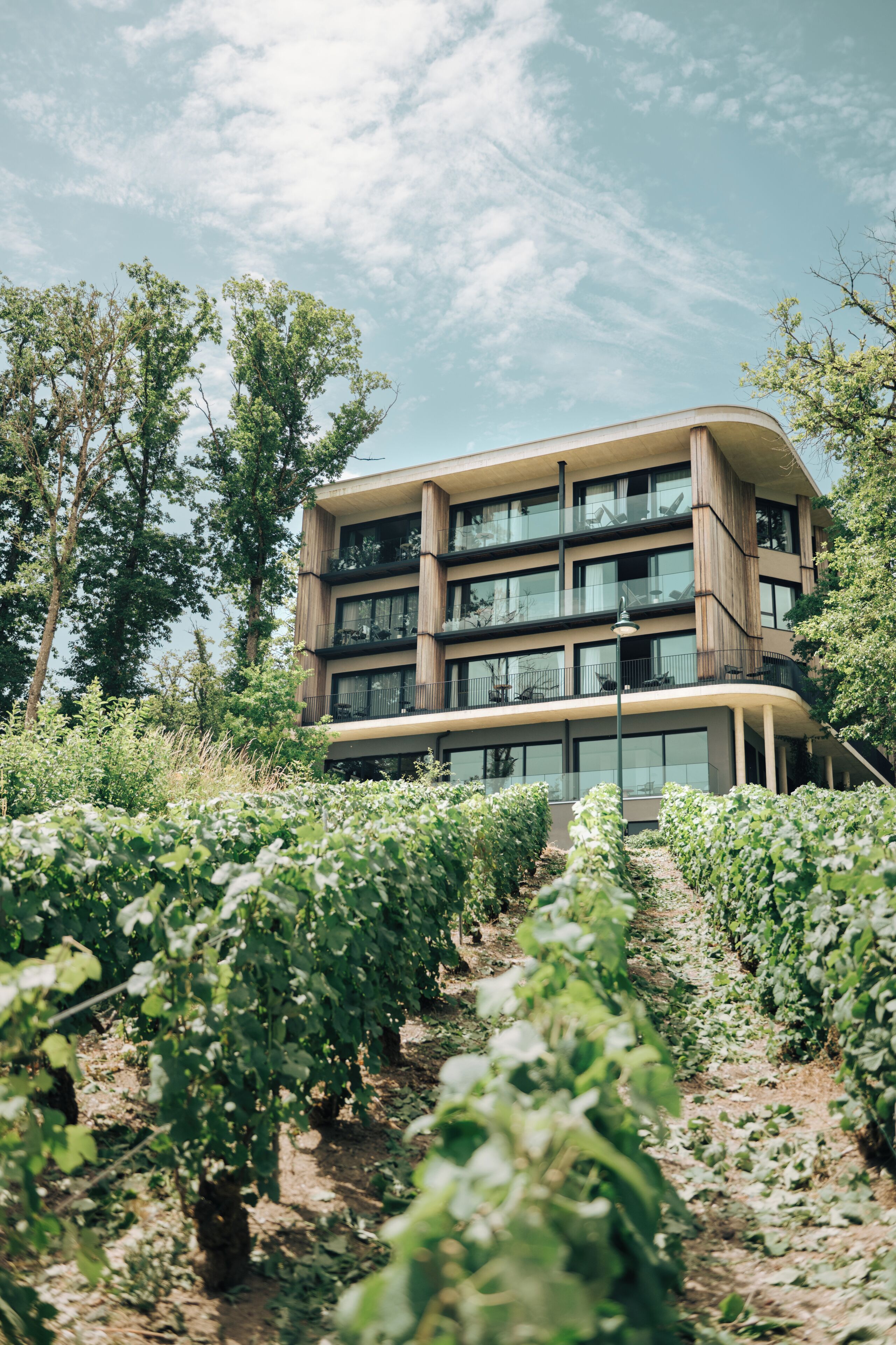 A multi-story building with balconies, surrounded by greenery and trees.