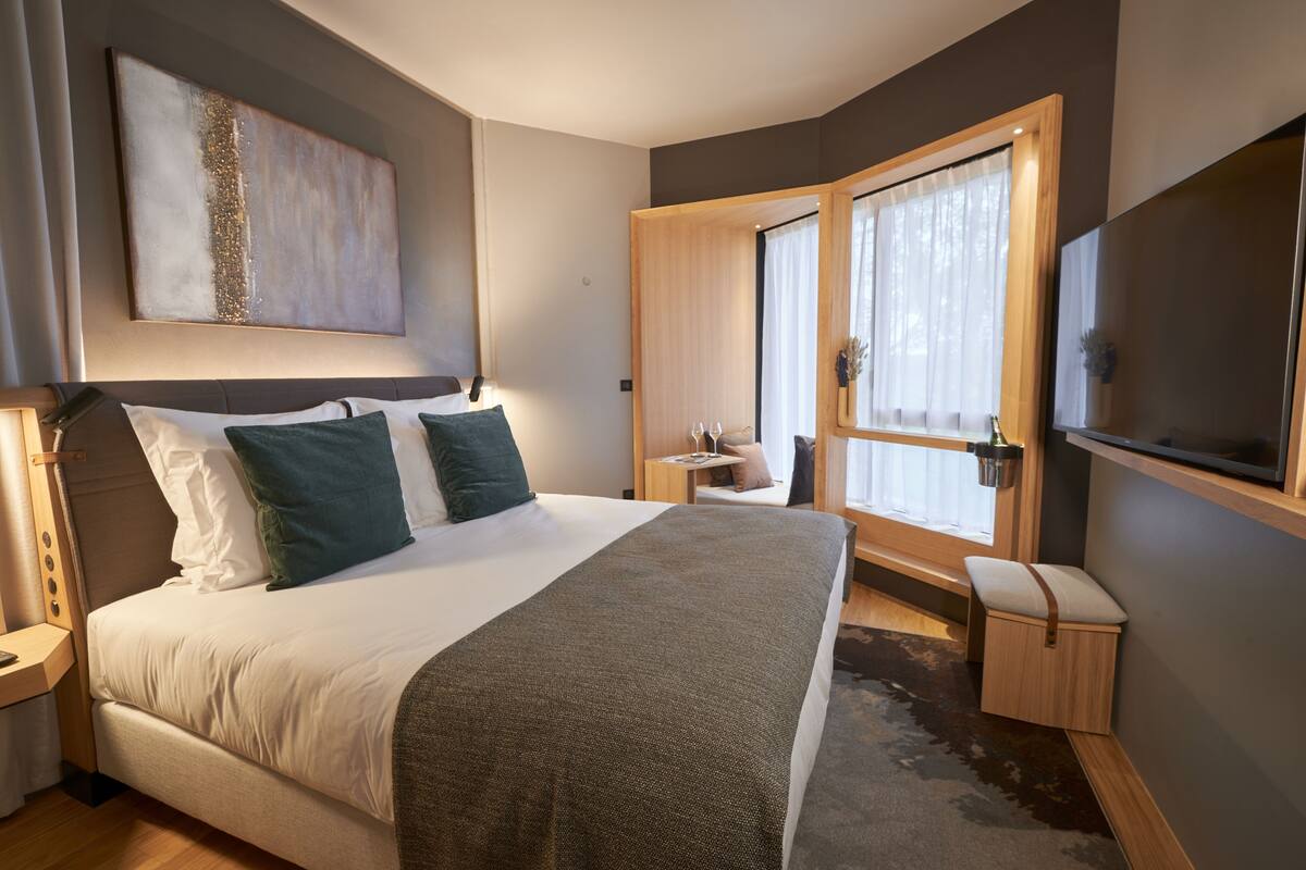 Een moderne hotelkamer met een groot bed, nachtkastjes, een klein bureau en een aan de muur bevestigde televisie.
