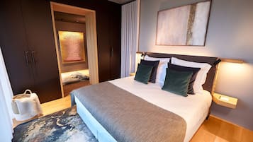 A modern hotel room with a large bed, a headboard with integrated lighting, a dark wardrobe, and a large abstract painting on the wall.