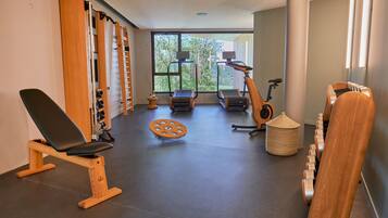 Un gimnasio con equipo de ejercicio, ventanas amplias y vistas a árboles.