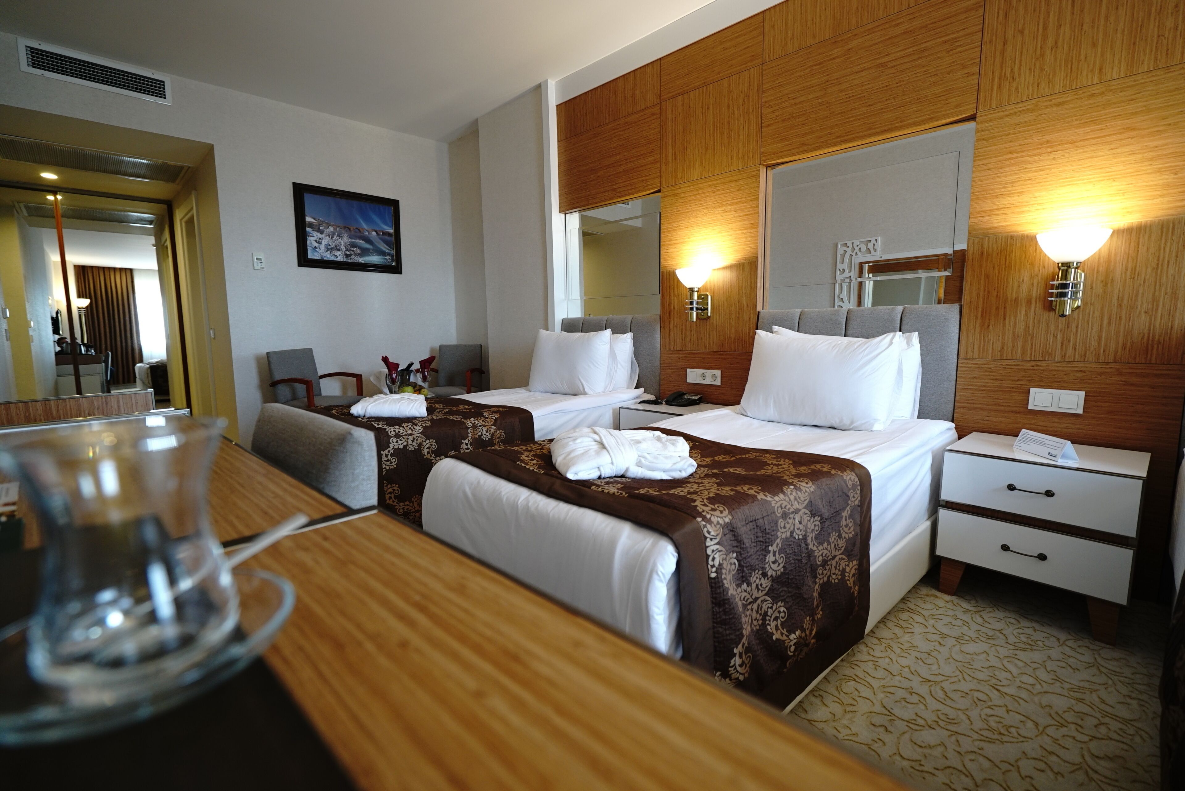 Habitación de hotel con dos camas, cabecera de madera, mesita de noche, escritorio y un espejo.