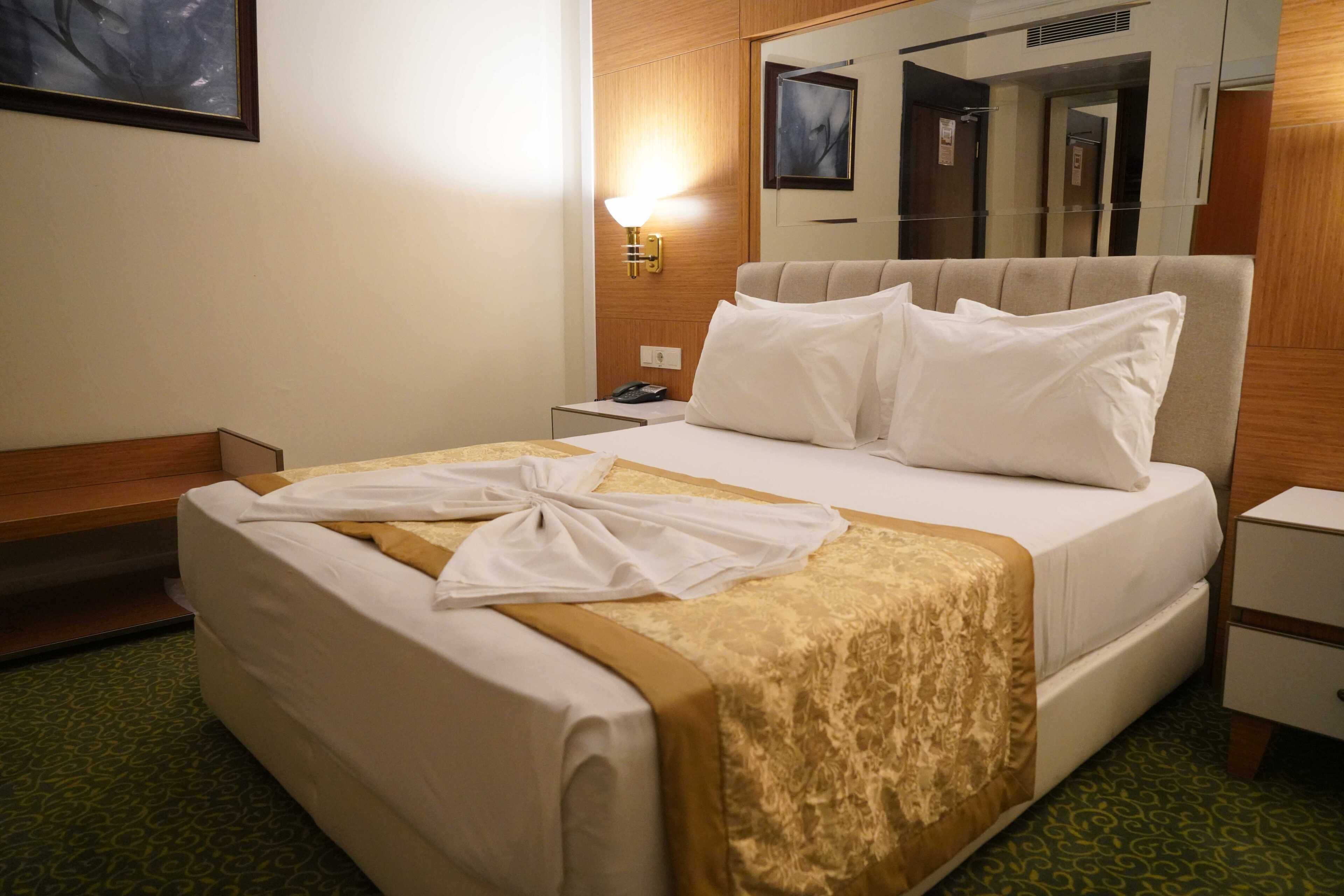 Una habitación de hotel con una cama, una mesita de noche, una lámpara y un espejo.
