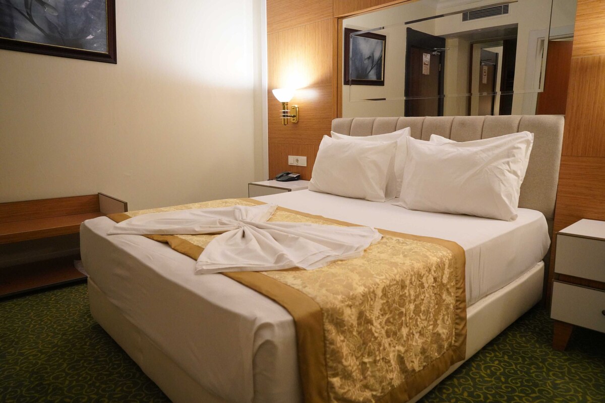 A hotel room with a bed, a nightstand, a lamp, and a mirror.