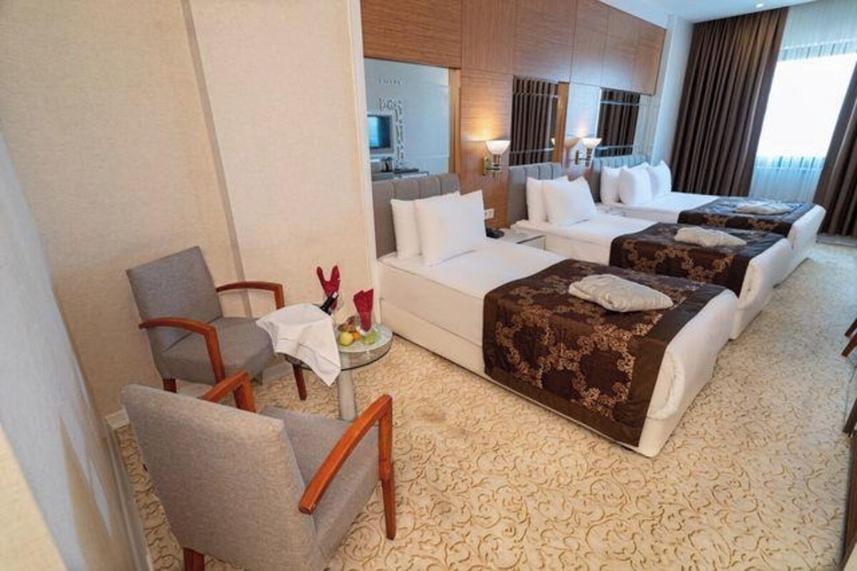A hotel room with a sofa bed, a single bed, a small table with a bottle and glasses, and a chair.