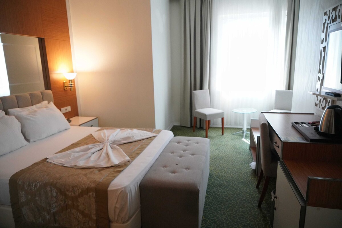 A hotel room with a bed, a desk, a chair, a small table, and a lamp.