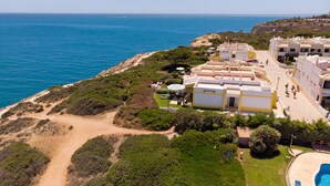 A coastal hotel with multiple buildings, a swimming pool, and a beach path.
