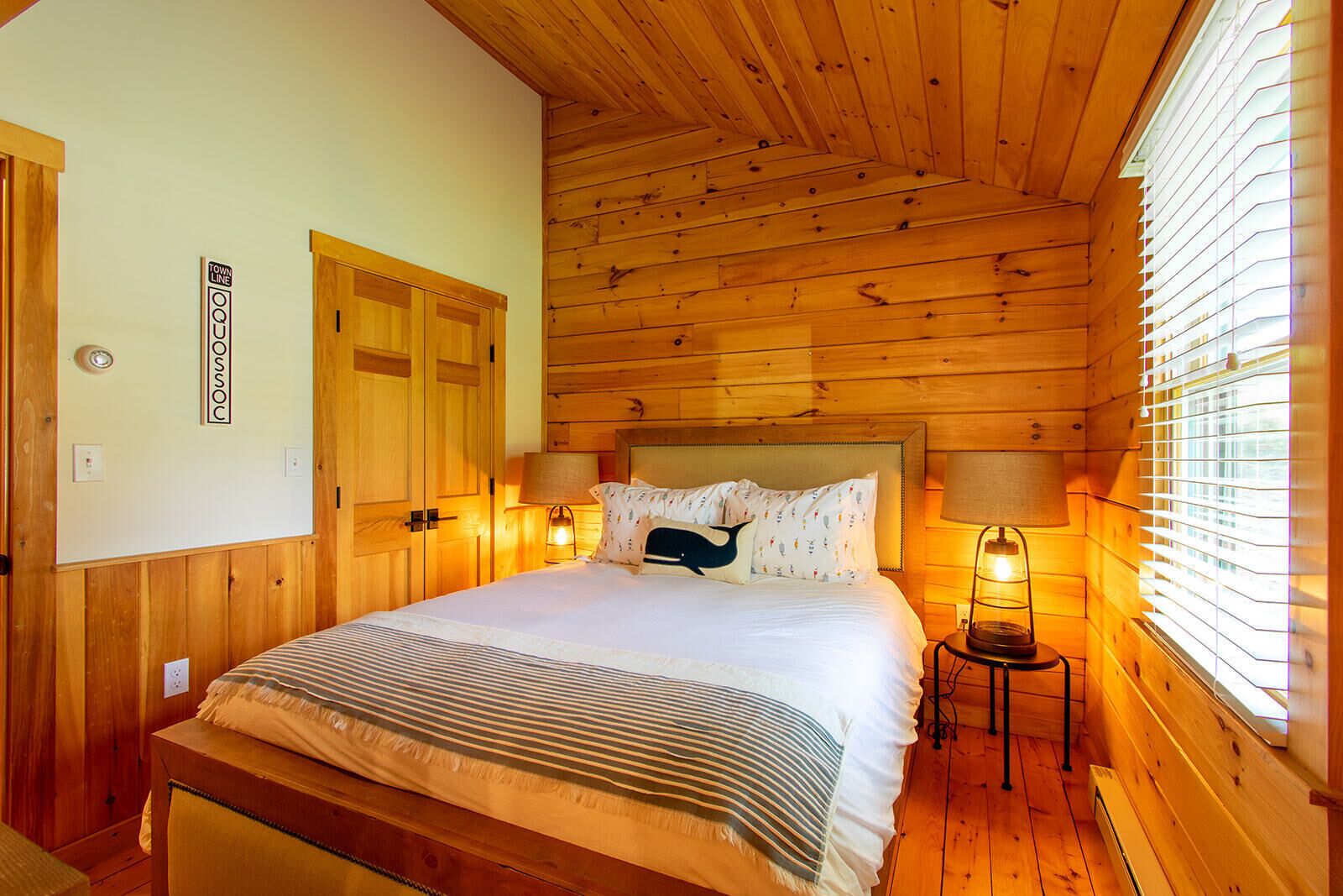 A wooden-paneled bedroom with a bed, bedside lamps, and a window with blinds.