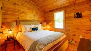 Een slaapkamer in een houten blokhut met een bed, twee bedlampjes, een raam en een decoratie aan de muur.