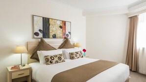 Ein Hotelzimmer mit einem ordentlich bezogenen Bett, einem Nachttisch mit Lampe, einem kleinen Tisch mit einer Vase und einem Gemälde an der Wand.