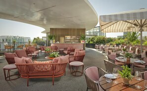 Un bar situé sur le toit, avec des meubles en osier, un comptoir et des plantes en pot.