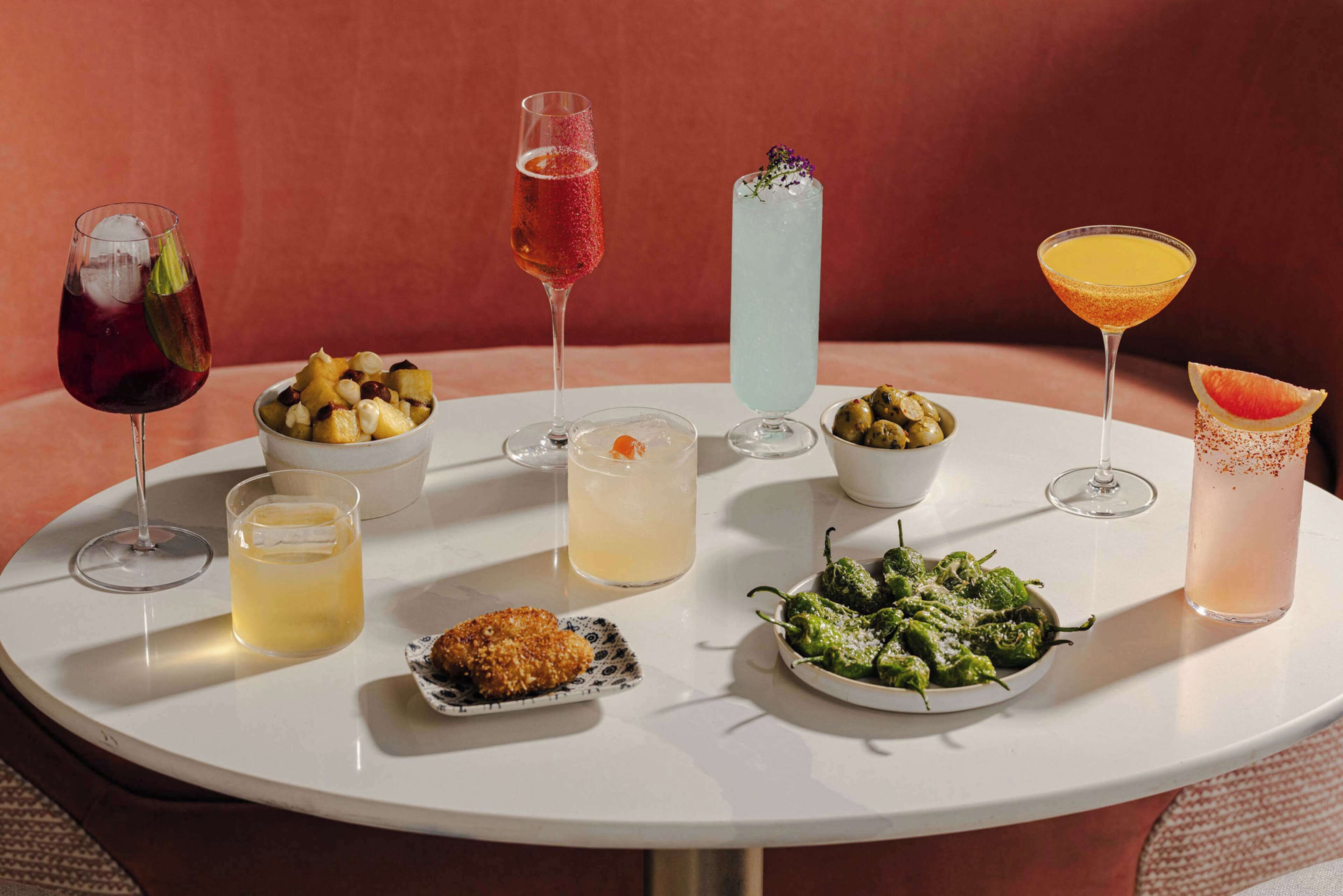 A round table with various drinks and dishes, including a martini, a cocktail with a fruit garnish, and a bowl of green vegetables.