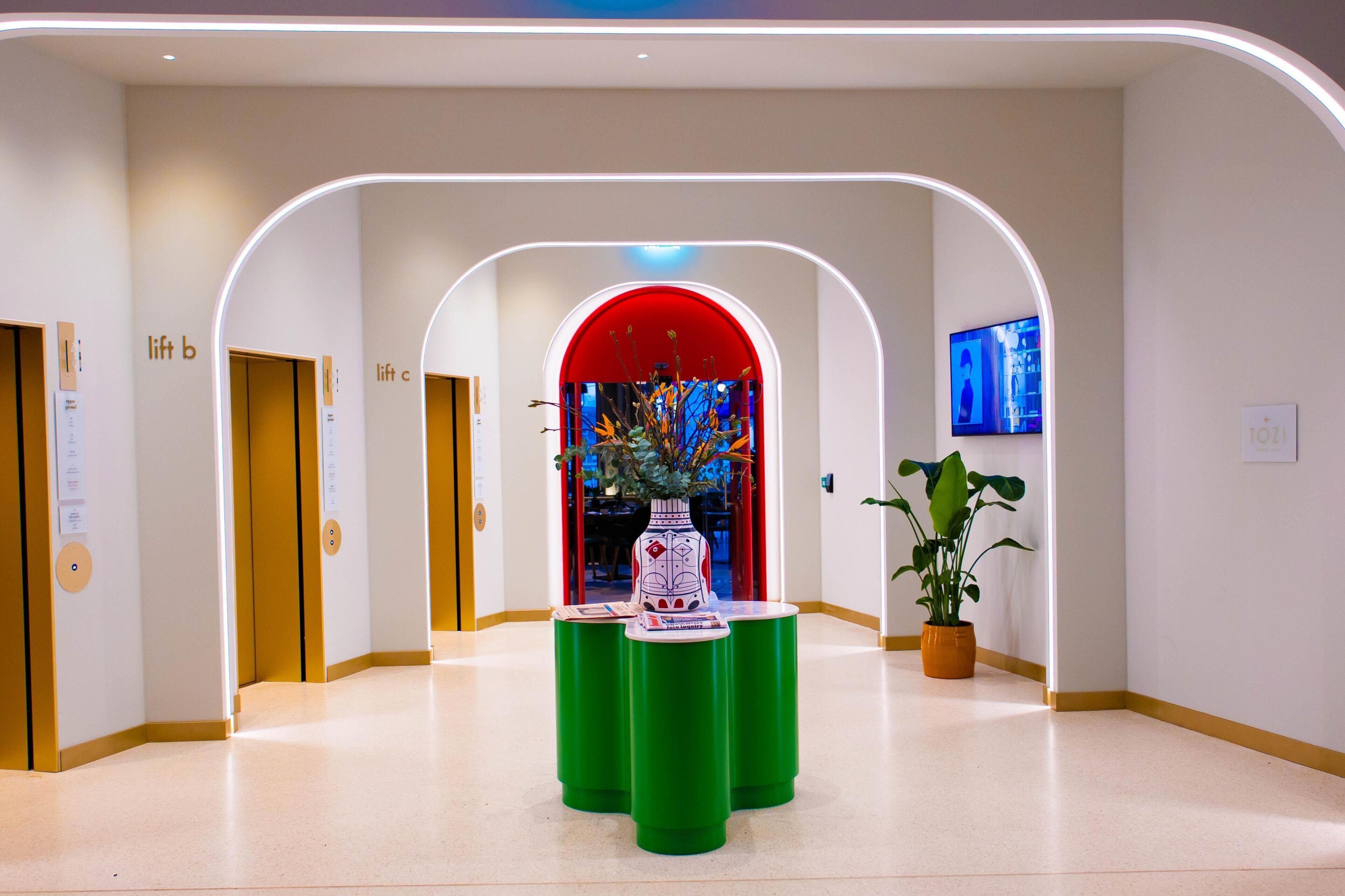 A modern interior with a central green table, a red archway, and a television screen on the wall.