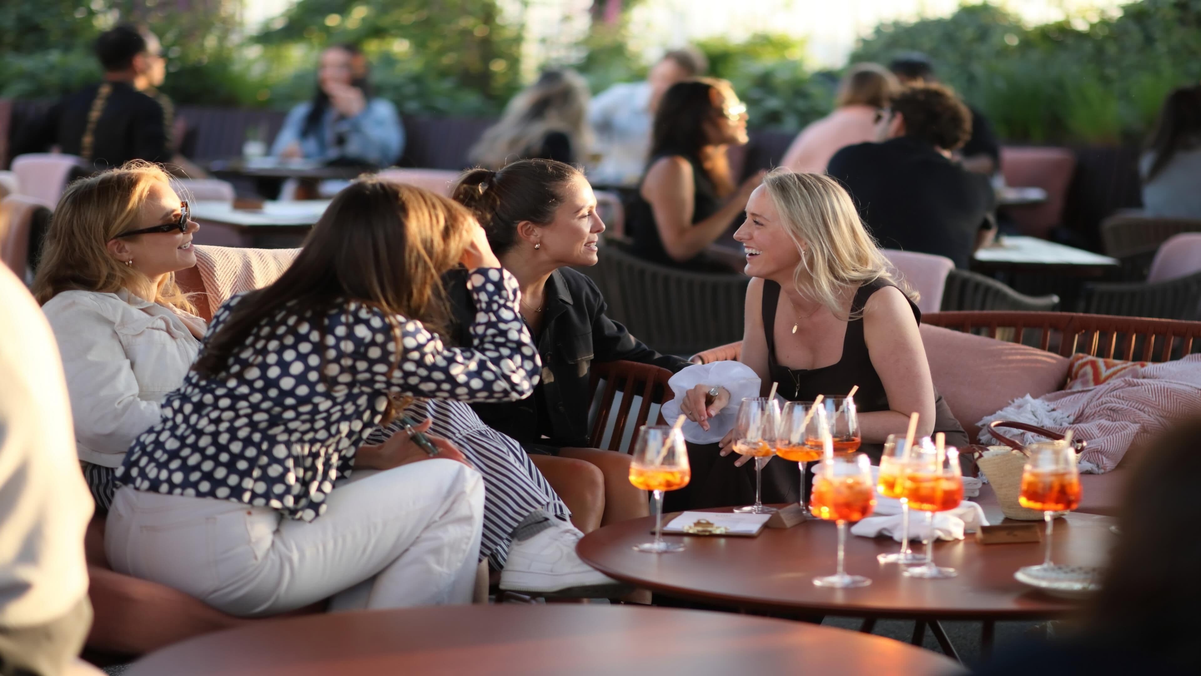 A group of people seated at an outdoor table with drinks, surrounded by greenery.