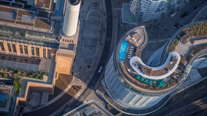 Vue aérienne d’un quartier urbain moderne, avec un bâtiment aux lignes courbes, une haute structure cylindrique et un rond-point agrémenté de verdure.