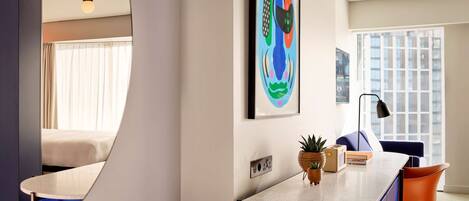 A modern hotel room with a curved counter, a bed, a large window, and a colorful abstract painting on the wall.