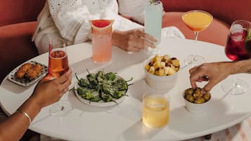 A round table with various drinks and food items, including a plate of green peppers, a bowl of fruit, and a glass of beer.