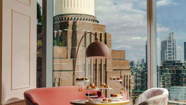 Une chambre moderne avec vue sur la ville, une table ronde garnie de pâtisseries et une grande fenêtre.