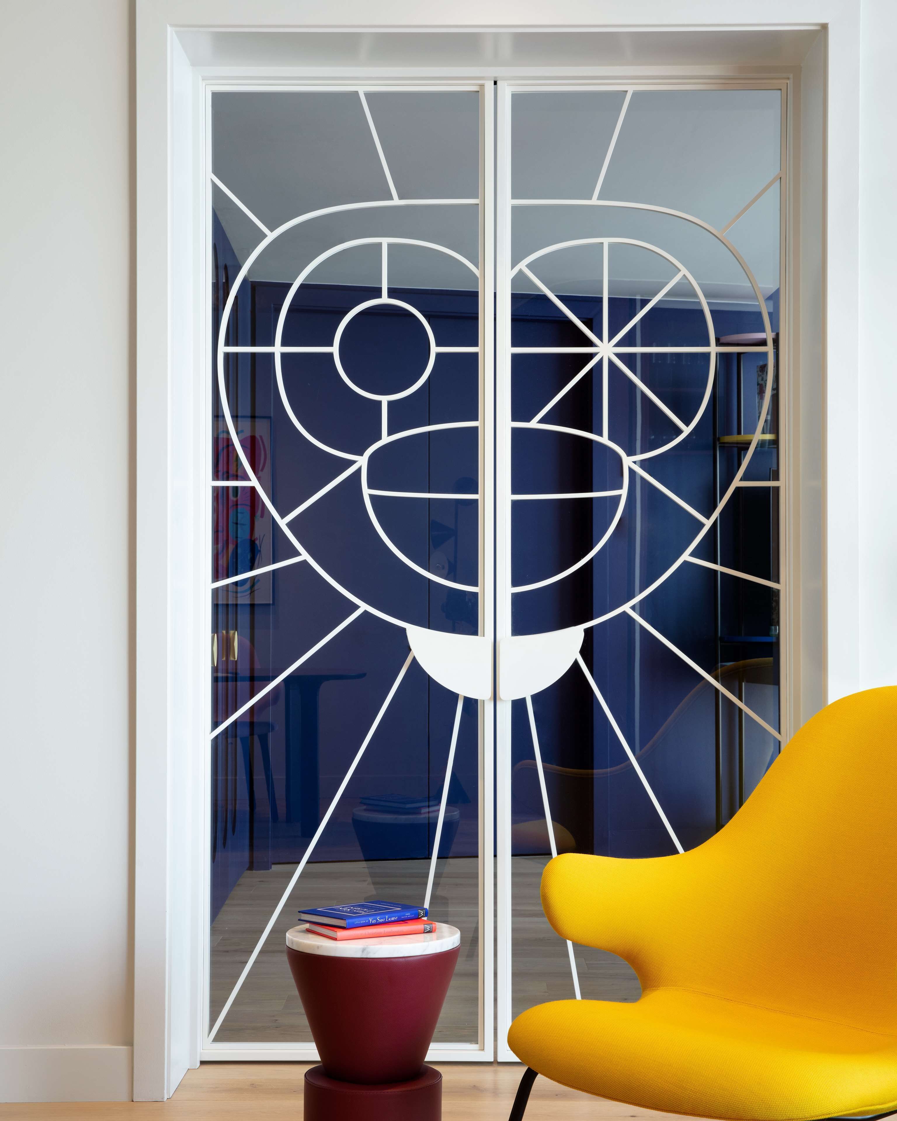 A room with a sliding glass door featuring a geometric design, a red and yellow chair, and a small table with books.