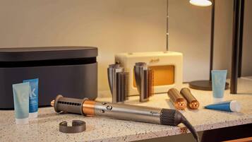 A bathroom vanity with a Dyson hair dryer, a hair straightener, and two tubes of hair care product.