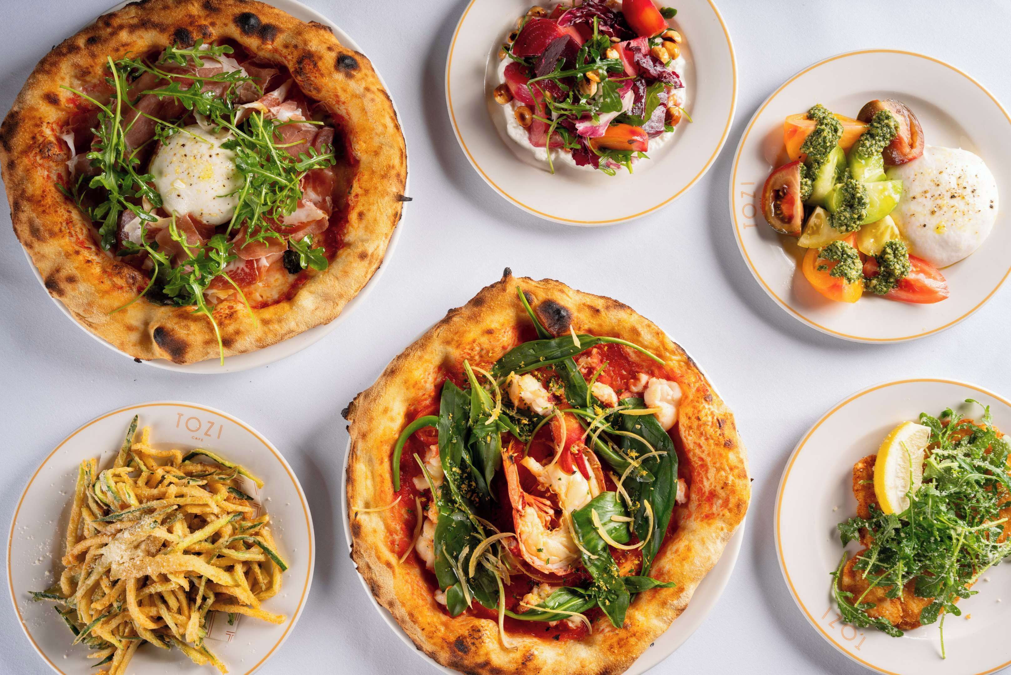A variety of dishes including pizzas and salads on plates.