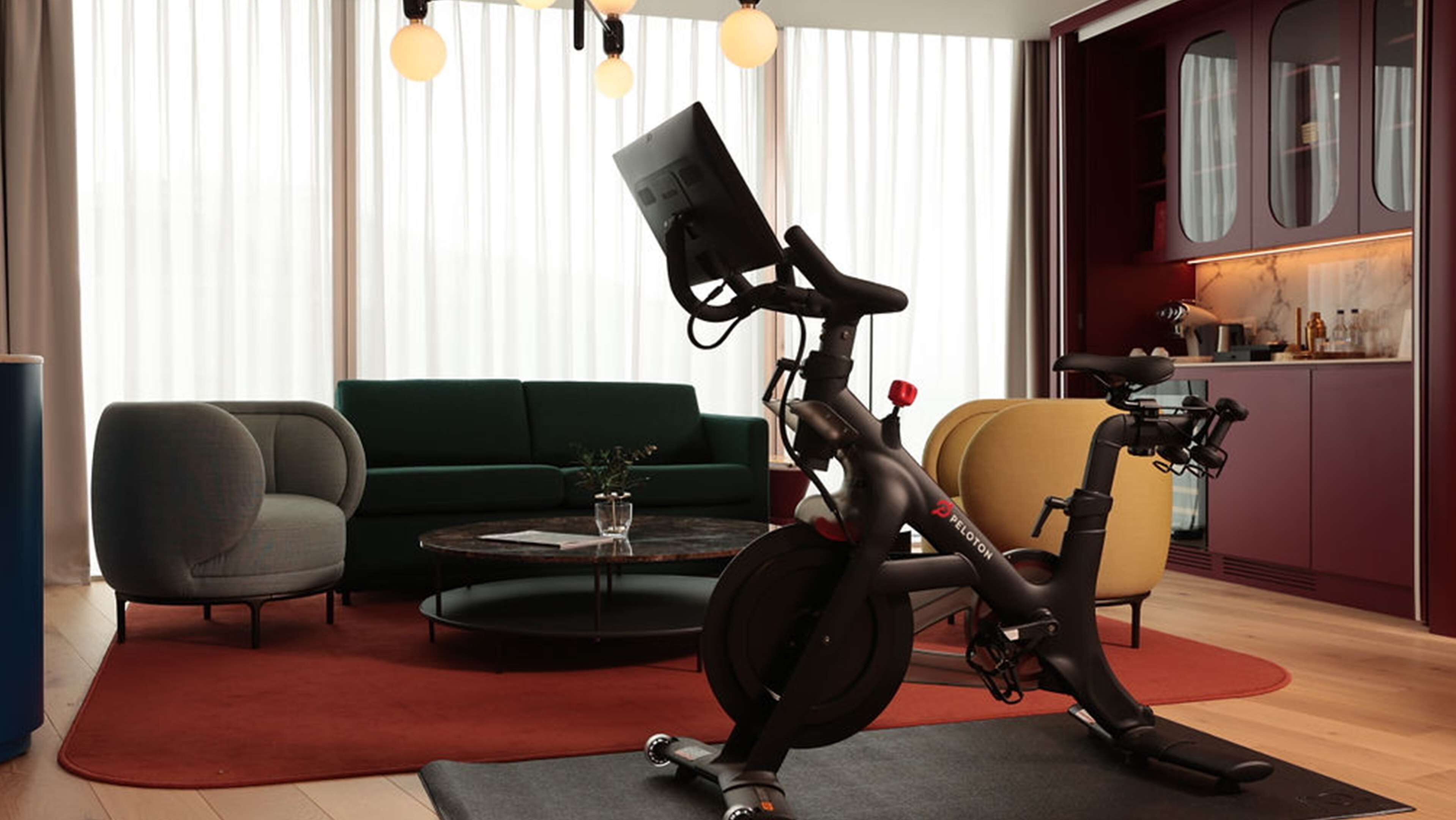 Ein modernes Wohnzimmer mit einem stationären Fahrrad, einem grünen Sofa, einem Couchtisch und einer Küchenzeile im Hintergrund.